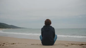 En person sitter alene på en strand, tapt i tanker, med et trist uttrykk i ansiktet.