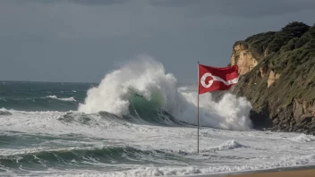 Et kystområde med en stor bølge som slår mot stranden, med et rødt varsel flagg som vifter i vinden.