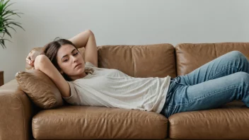 En person som ligger på en sofa, omgitt av snacks og fjernkontroller, med et lat uttrykk i ansiktet.