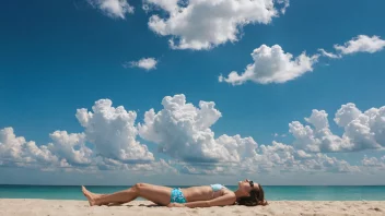 En person som solbader på en strand, omgitt av en klar blå himmel og noen få hvite skyer.