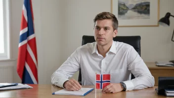 En person som sitter ved et skrivebord med et norsk flagg i bakgrunnen.